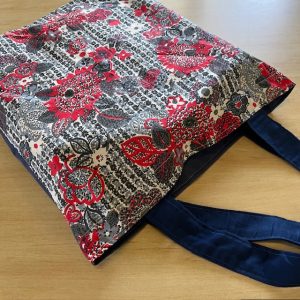 Bag with elegant red flowers with back and white pattern in the background. Dark blue handles