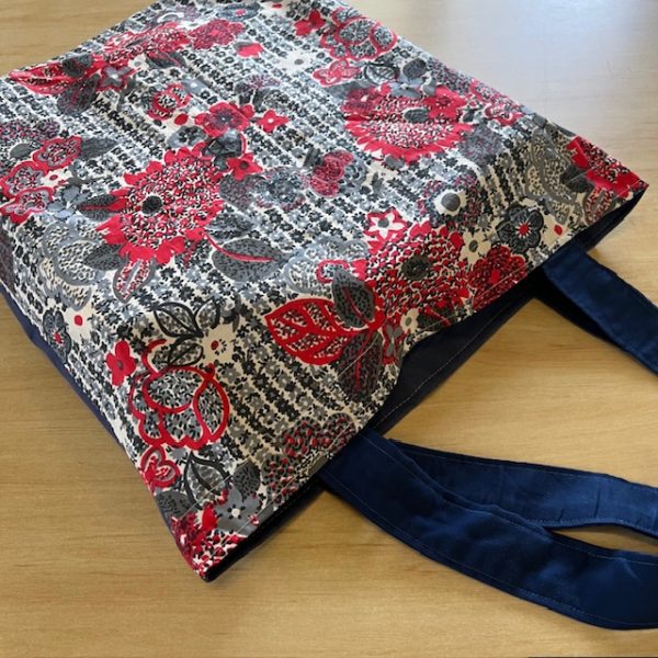 Bag with elegant red flowers with back and white pattern in the background. Dark blue handles