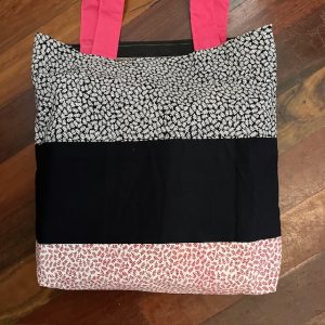 Bag with pink handles. Made with three distinct fabrics: white with red leaves, black, and white with black leaves.