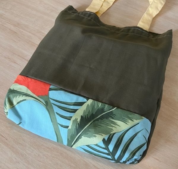 Bag with light yellow straps, deep green body with a panel of blue tropical fabric at the bottom