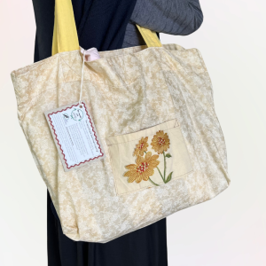 Cream coloured bag with subtle flower pattern. Pocket with embroidered daisies on the front. Yellow handles